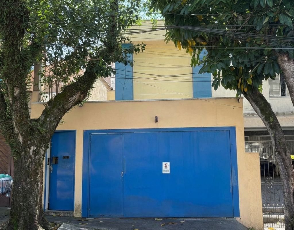 Fachada de kitnet disponível para alugar em Pinheiros, São Paulo, com portão azul e árvore na calçada